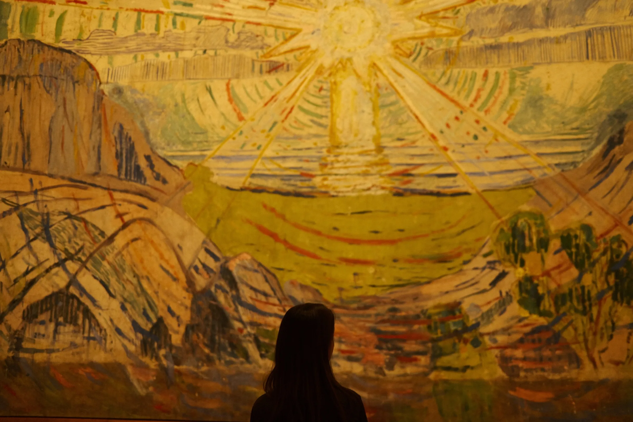 A person looking up at a large, colourful painting of a sun in a museum.